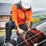 Man technician mounting photovoltaic solar panels on roof of house with help of hex key.